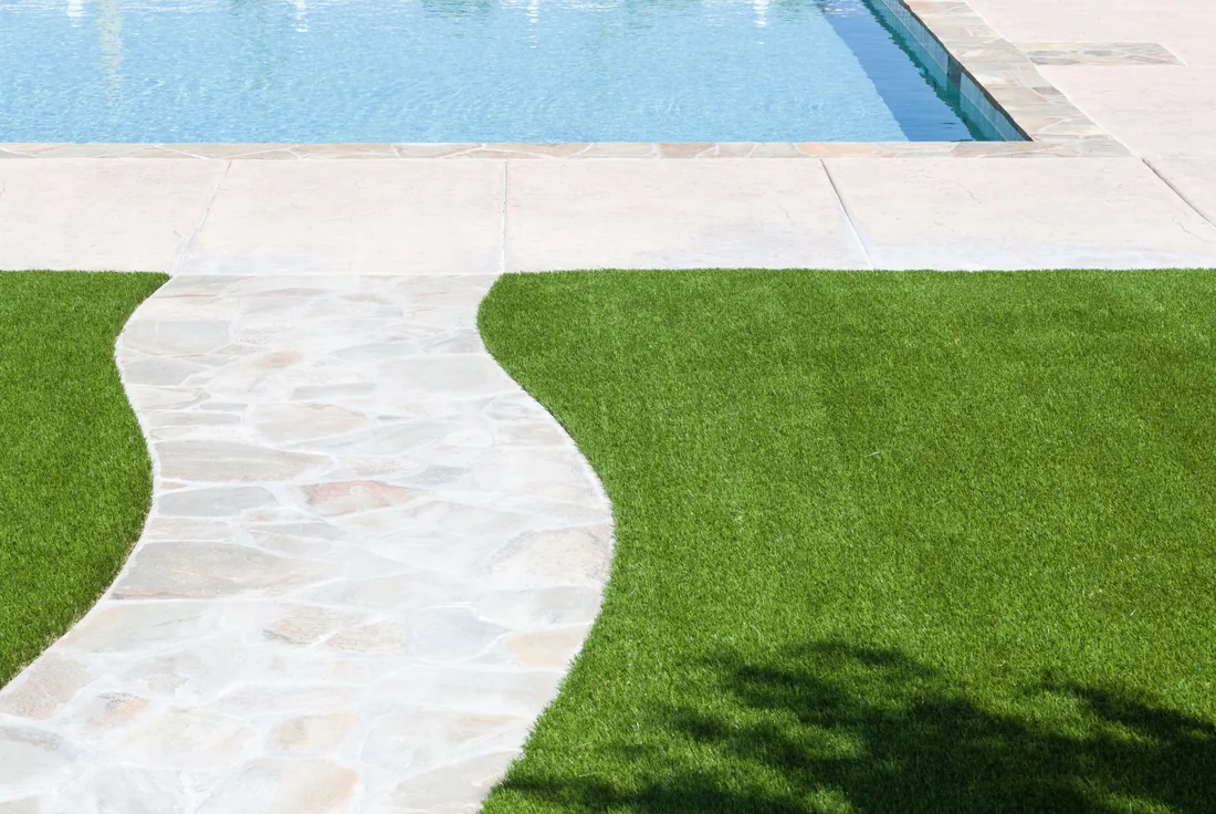Artificial turf laid flush against pool coping and a curved stone paving path